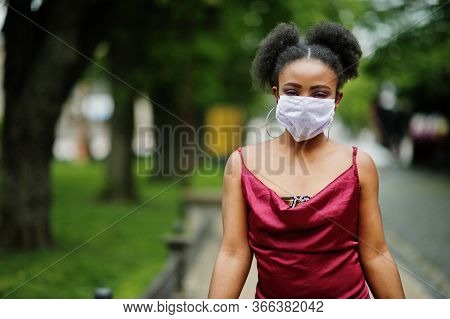 Covid-19, Infectious Virus. African Woman With Curly Hair, Wears Red Silk Dress And Medical Disposab