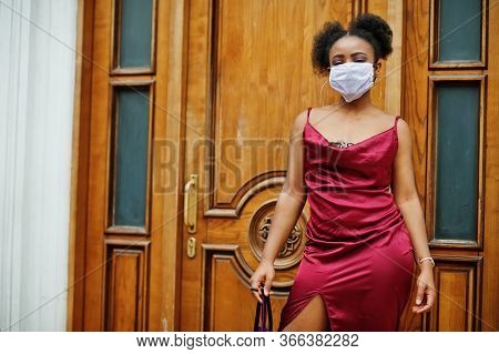 Covid-19, Infectious Virus. African Woman With Curly Hair, Wears Red Silk Dress And Medical Disposab