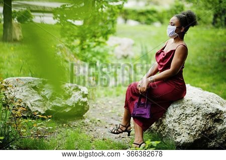 Covid-19, Infectious Virus. African Woman With Curly Hair, Wears Red Silk Dress And Medical Disposab