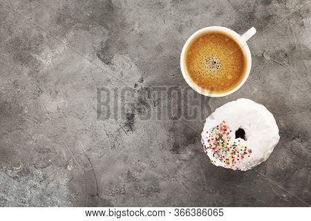 White Cup Of Coffee And Donut In White Icing And Multicolored Sugar Pastry Topping On Grey Backgroun