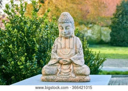Buddha Statue With Closed Eyes In The Lotus Position Against The Background Of Bushes. Old Clay Budd