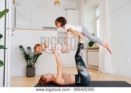 Mom Doing Gymnstics With Her Kids On A Yoga Mat At Home