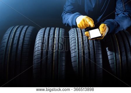 New Tires Selection Concept With Worker Hands With Empty Smartphone Screen And Set Of New Tires.