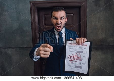 Angry Collector With Documents With Foreclosure Lettering Pointing With Finger And Shouting In Room