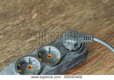 Used Electric Extension Cord On A Wooden Table. Black Developer With A Plug In The Plug. Electrical 