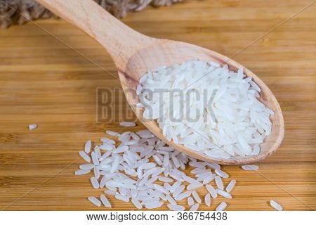 Uncooked Long Grain Basmati Rice In The Wooden Spoon On And Scattered Beside On The Wooden Surface W