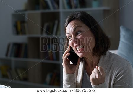 Angry Adult Woman Calling On Smart Phone Sitting In The Living Room At Night At Home