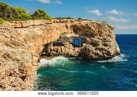 View on rocks with hole and deep blue sea at Cala Sa Nau beach and Cala d'Or city. Mallorca island, Spain Mediterranean Sea, Balearic Islands.