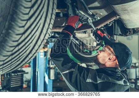 Male Car Technician Using Wrench To Fasten Parts Of Undercarriage Of Vehicle.