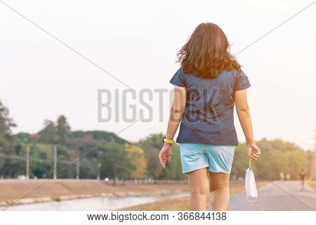 Sportive Woman Take Off Protective Mask While Jogging For Easier Breathing On Road Beside Irrigation