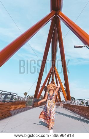 Carefree Smiling Woman Walking Vicaciously Across A Modern Foot Bridge Across The River