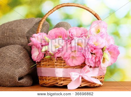 Blumenstrauß Eustoma in Korb, auf Holztisch, auf grünem Hintergrund