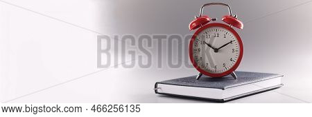 Close-up Of Red Retro Clock Stand On Top Of Closed Book Or Diary, Time To Study, Time To Learn New I