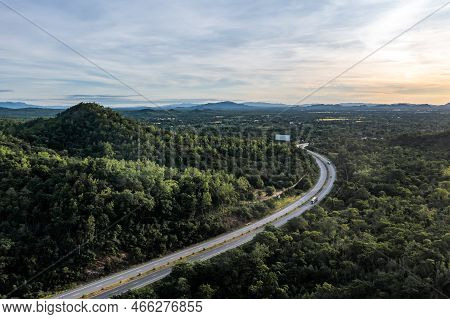 Aerial Landscape Of 4 Lane Road With Residential Area, Forest, Mountain,  Blue Sky And Sunlight With