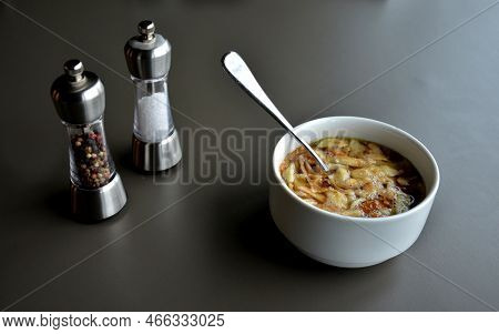 Spoon In Bowl With Soup On Gray Table In Restaurant. Salt And Pepper To Season The Food. Porcelain B