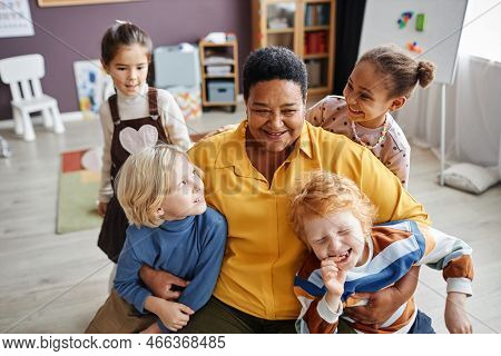 Happy Mature African American Teacher Of Nursery School Embracing Two Adorable Boys While Having Fun