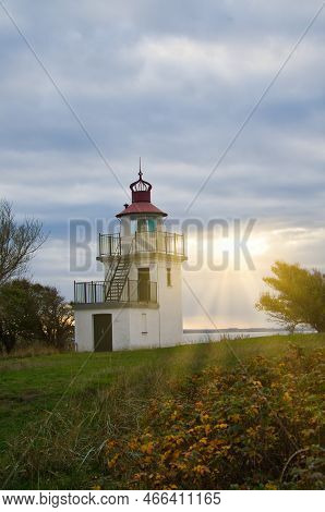 Lighthouse, Spodsbjerg Fyr In Huntsted On The Coast Of Denmark. Sun Rays Shining Through The Clouds.
