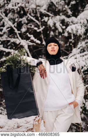 A Girl In A White Suit And Balaclava With A Package Of Christmas Trees In The Winter Forest On New Y