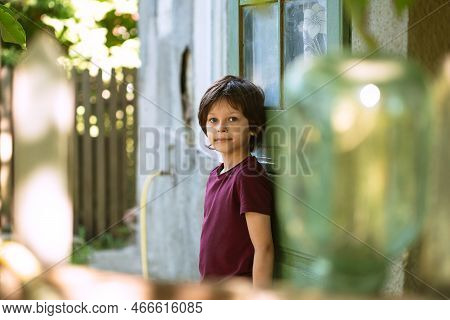 Portrait Of A Smiling White Boy Standing Near The Farm House Spending Summer Holidays In Countryside