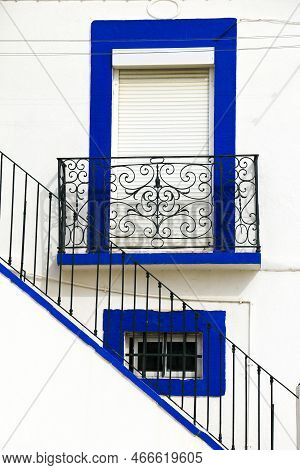 Typical Portuguese Whitewashed Facade And Stairs With Blue Painted Window And Forged Metal Balcony