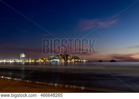 A Mazatlan Sinaloa Beach At Night With Luminous City In The Background