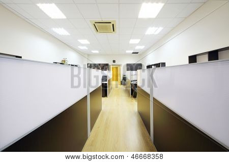 Corredor e áreas de trabalho vazio com desktops separados por divisórias no escritório.