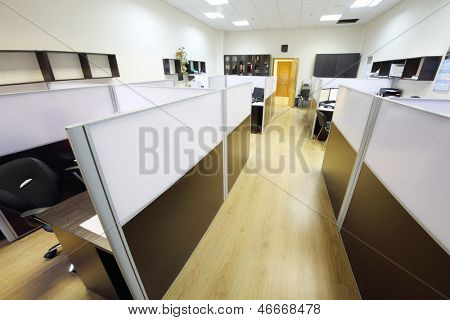 Corredor com piso de madeira e áreas de trabalho vazio com desktops no escritório.