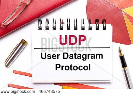 On The Desktop Is A White Notebook With The Text Udp User Datagram Protocol, A Pen, Burgundy And Red