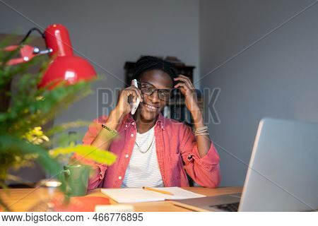 Friendly Smiling Young African Man Remote Worker Making Call Using Mobile Device While Working At Ho