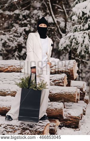 A Girl In A White Suit And Balaclava With A Package Of Christmas Trees In The Winter Forest On New Y