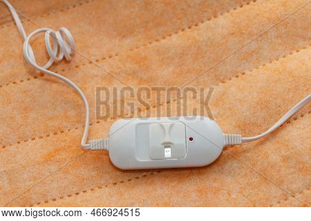 A Warm Orange New Electric Sheet, Lies Assembled, And On Top Of The Sheet Lie A White Temperature Sw