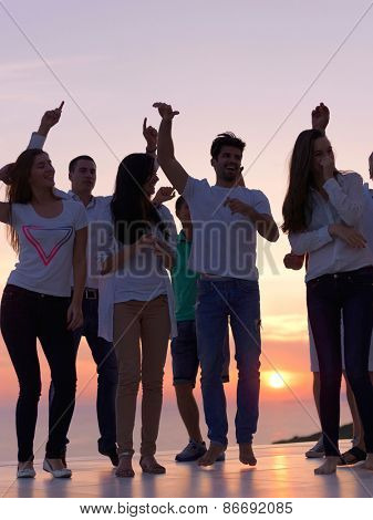 group of happy young people dancing and have fun on party in modern home bacony with sunset and ocean in background