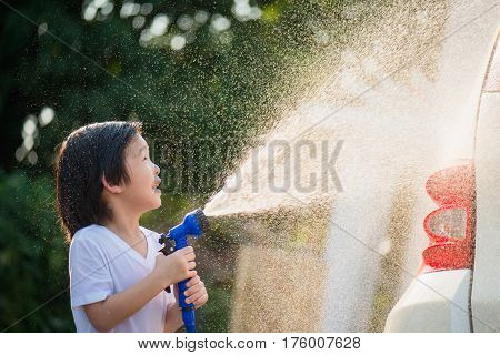 Asian child washing car in the garden on summer day