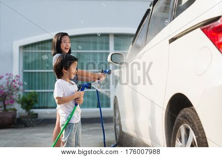 Asian girl washing car in the garden on summer day