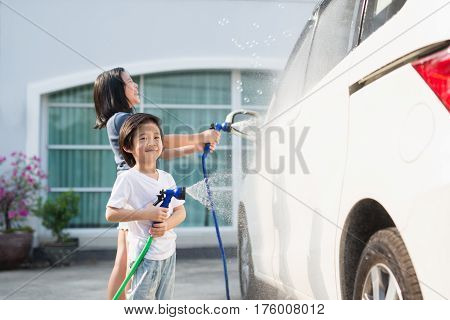 Asian children washing car in the garden on summer day