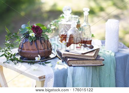 Cocolate cake decorated with flowers and three whiskey decanters against a light gray background with copy space