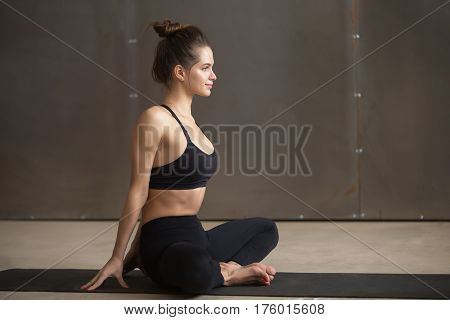 Young attractive smiling yogi woman practicing yoga, sitting in baddha konasana exercise, Butterfly pose, working out, wearing black sportswear, cool urban style, full length, grey studio background
