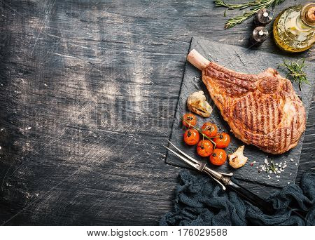 Succulent grilled tomahawk beef steak on the bone with seasonings, fresh rosemary and grilled vegetables on a black background, top view