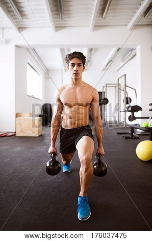 Fit hispanic man doing strength training, doing lunges with kettlebells in crossfit gym
