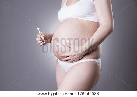 Pregnant woman making injection in stomach close-up studio shot on gray background