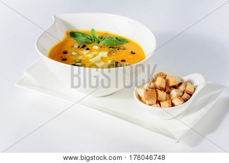 Roasted pumpkin soup with cream and pumpkin seeds on white background. Copy space.