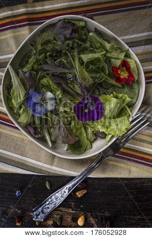 Spring green salad with edible flowers over a dark table