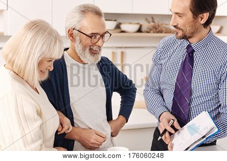Choosing variants of investment. Qualified positive upbeat realtor talking to aging couple of clients while presenting the contract for apartment investment and expressing joy