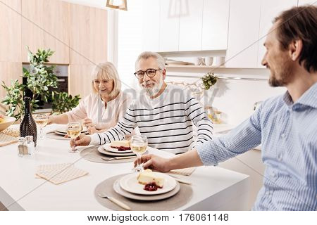 Enjoying cozy family dinner . Charismatic optimistic cheerful aged couple having dinner and enjoying weekend with their mature son while holding glasses full of champagne