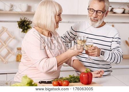 Expressing our feelings. Smiling cheerful merry aged couple standing in the kitchen and preparing dinner while expressing positivity and drinking champagne