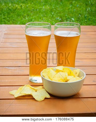 Light beer with potato chips on wooden table