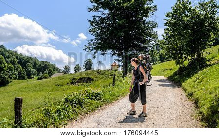 Mother With Baby In Backpack Carrier Is Hiking In Mountains.