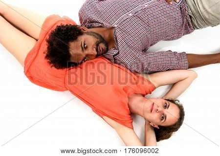 Interracial couple is lying on the floor embracing their love. African American black man wearing stripped shirt is in love with Caucasian white woman wearing a pink dress. A young couple in love.