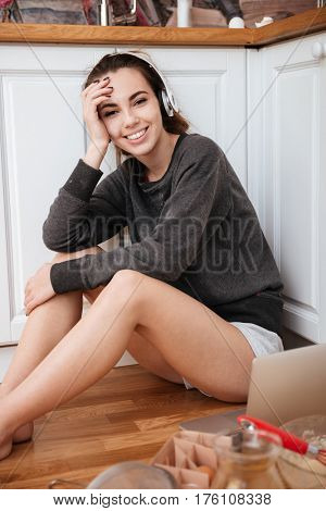 Portrait of a young pretty girl in headphones cooking beakfast while sitting on a kitchen floor