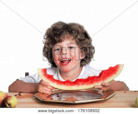 Happy cute curly-haired boy looks at the camera with a piece of large ripe watermelon in his hands. Blue background. Close-up.